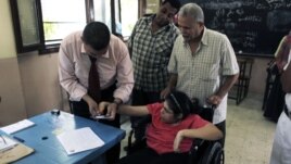 An Egyptian election worker helps a disabled woman in a wheelchair to vote at a polling station during the second day of the presidential runoff in Cairo, June 17, 2012.