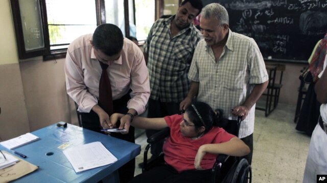 An Egyptian election worker helps a disabled woman in a wheelchair to vote at a polling station during the second day of the presidential runoff in Cairo, June 17, 2012.