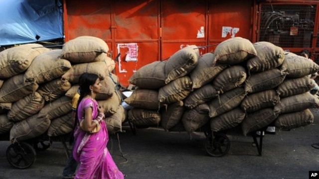 An Indian woman walk past carts loaded with sacks of food items at a wholesale market in New Delhi, India, June 9, 2011. 