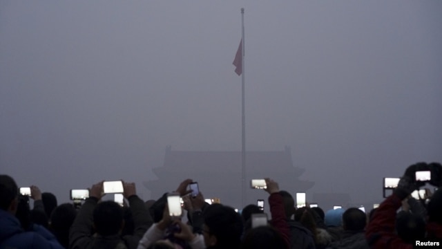 Visitors use mobile phones to take pictures and videos as they watch a flag raising ceremony at the Tiananmen Square amid heavy smog in Beijing, China.