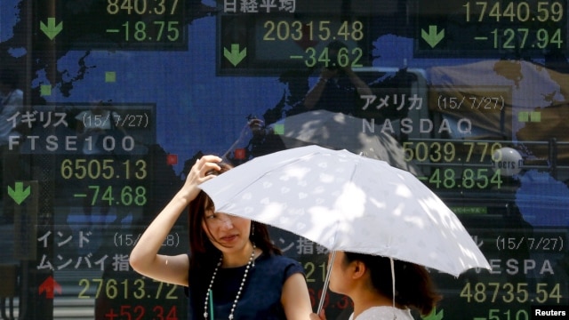 FILE - Women stand in front of a board showing market indices in Tokyo July 28, 2015.