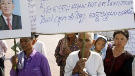 Sam Souen, an 86 year-old Cambodian woman, holds a banner asking Prime Minister Hun Sen, seen in photo at left, to help solve the problem of land grabbing.