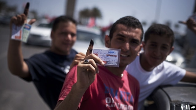 Libyan men hold their elections ID cards while celebrating election day in Tripoli, Saturday, July 7, 2012. 
