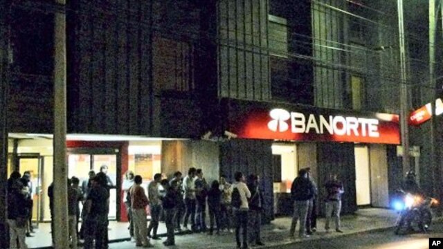 People stand on a sidewalk outside a building in Mexico City after an earthquake, December 10, 2011.