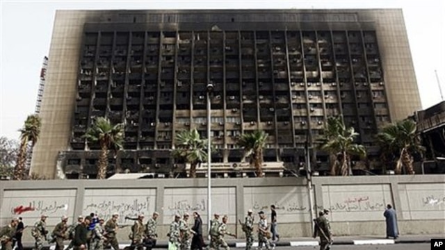 Army soldiers march in front of the burned down building of former President Hosni Mubarak's National Democratic Party in Cairo, Egypt, February 15, 2011