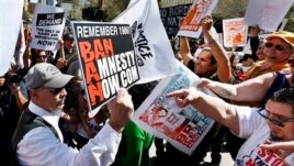 An anti-immigration rights protester, left, holds up a sign as he is pointed at and shouted at by immigration rights marchers during a Puente Movement event March Against Deportation, Family Separation, and Workplace Raids on March 11, 2013, in Phoenix.