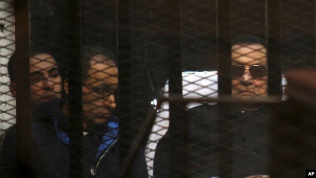 Ousted Egyptian President Hosni Mubarak, 86, lies on a journey, next to his son Gamal, second left, in the defendants cage, during a court hearing in Cairo, Egypt, Saturday, Nov. 29, 2014.