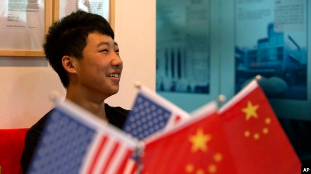 FILE - 16-year-old Zhang Kaisheng smiles near Chinese and U.S. national flags at the lobby of Focus Education, a tutoring and consulting agency in Beijing.