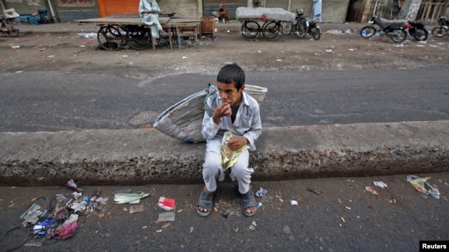 A child sits along a road median as he eats his breakfast of a single piece of "roti" (South Asian bread) while waiting for work in Karachi early morning May 6, 2012.