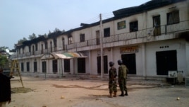 In this photo taken with a mobile phone, soldiers stand outside a burnt out shopping mall in Maiduguri, Nigeria, Monday, Oct. 8, 2012.