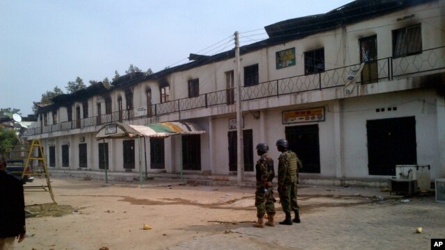 In this photo taken with a mobile phone, soldiers stand outside a burnt out shopping mall in Maiduguri, Nigeria, Monday, Oct. 8, 2012.