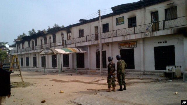 In this photo taken with a mobile phone, soldiers stand outside a burnt out shopping mall in Maiduguri, Nigeria, October 8, 2012.