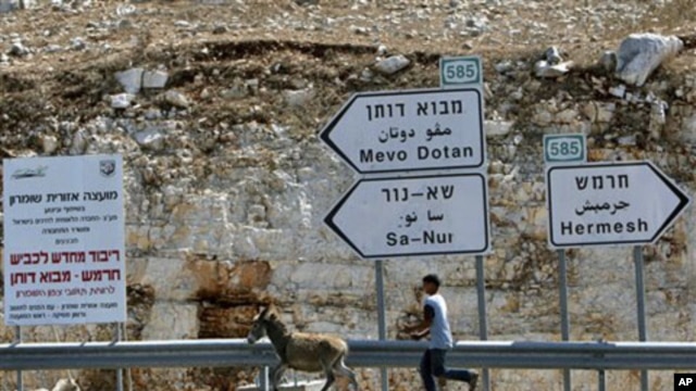 A Palestinian youth leads a donkey next to signs leading to Jewish settlements in the northern West Bank, 27 Sep 2010