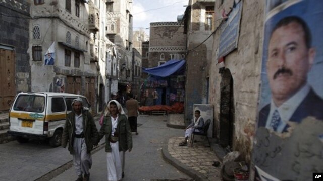 People walk along a street where posters hang of Yemen's President Ali Abdullah Saleh in the old city of Sanaa, Yemen, August 7, 2011