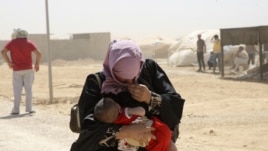 A Syrian refugee woman carries her baby as they walk amidst dust at the Al Zaatri refugee camp in the Jordanian city of Mafraq, near the border with Syria, August 13, 2012.