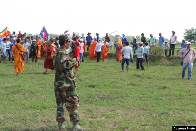 Nhiều người Việt đội mũ bảo hiểm, cầm gậy gộc và súng đứng đối diện với sư sãi và người Campuchia cầm quốc kỳ.