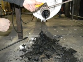 Many different types of unwashed plastic waste are melted together in a combustion chamber. Here, John Bordynuik, CEO of JBI, Inc., pulls a sample to determine what kind of fuel he wants to produce. (VOA/D. Robison)
