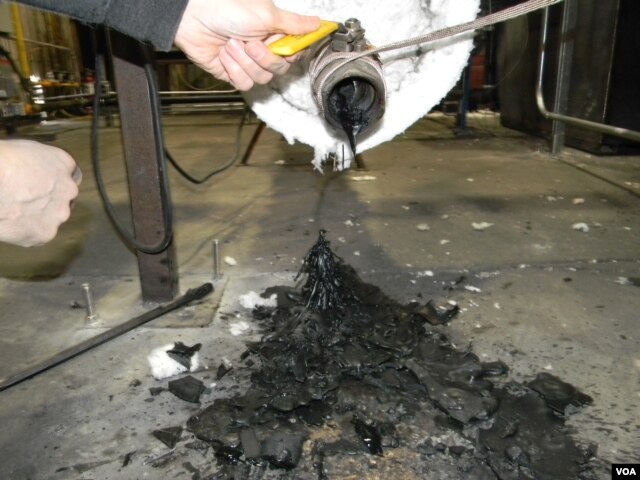Many different types of unwashed plastic waste are melted together in a combustion chamber. Here, John Bordynuik, CEO of JBI, Inc., pulls a sample to determine what kind of fuel he wants to produce. (VOA/D. Robison)