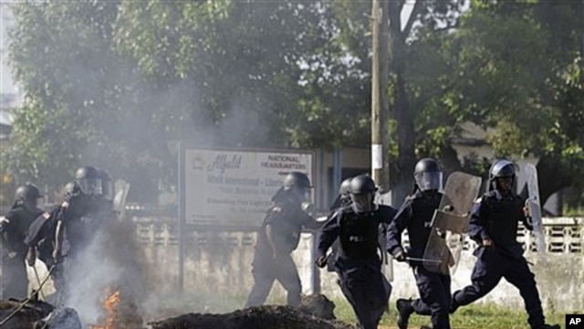 Liberian police advance past burning barricade as they chase opposition party supporters in Monrovia, Nov. 7, 2011.