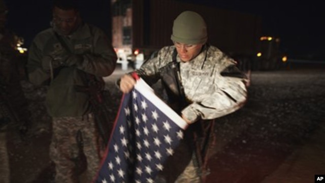 A soldier with the 3rd Brigade Combat Team, 1st Cavalry Division folds up a U.S. flag outside their Mine Resistant Ambush Protected (MRAP) vehicle before leaving Camp Adder near Nasiriyah to travel with the last U.S. military convoy to leave Iraq Sunday, 