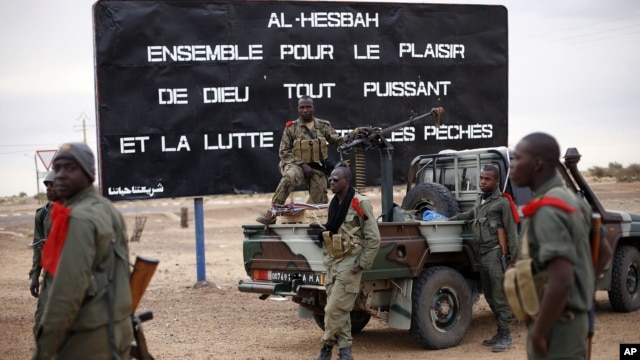 Malian soldiers are stationed at the entrance of of Gao, northern Mali, Jan. 28, 2013. The sign, a reminder of Islamic extremists, reads "Al Hesbah, together for the pleasure of God almighty and the struggle against sins."
