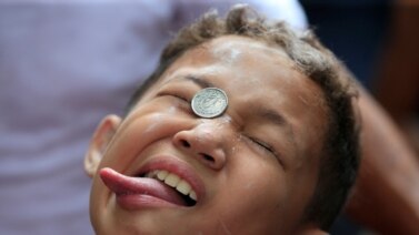 A boy attempts to move a coin into his mouth during a celebration of the patron saint Santa Rita de Cascia in Baclaran, Paranaque city, metro Manila, Philippines.