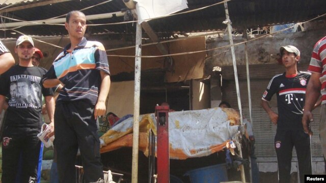 Men stand next to wreckage of car and scattered vegetable at market where a car bomb exploded in Diwaniya province, south of Baghdad, July 23, 2012.
