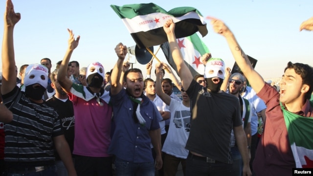 Syrian protesters wave Syrian opposition flags as they shout slogans against Syrian President Bashar Al-Assad outside the Syrian embassy in Amman, July 5, 2012.