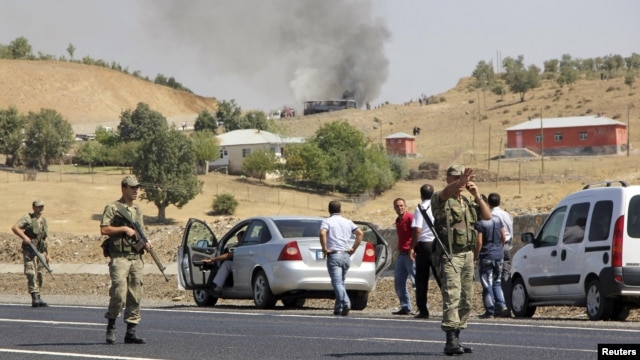 Turkish soldiers take security measures on a main road which connects eastern Turkish cities Bingol and Mus, as smoke rises from a burning vehicle attacked by PKK in the background, September 18, 2012. 