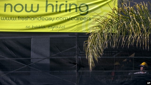 Un trabajador de la construcción junto a un letrero que anuncia nuevas contrataciones en Los Angeles.