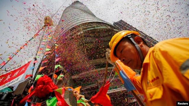 A worker attends the topping out ceremony as crane lift the last piece of steel at the Shanghai Tower, which is undergoing construction at the financial district of Pudong in Shanghai Aug. 3, 2013.