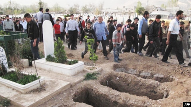 Mourners walk past open graves during a funeral for four people killed in a government raid on a Damascus neighborhood Thursday