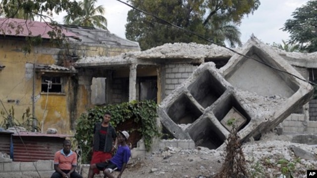 People sit outside a house that was destroyed by the January 2010 earthquake in Port-au-Prince, January 3, 2012.