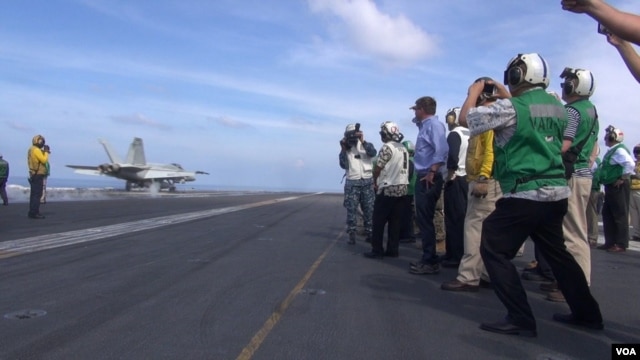 U.S. Secretary of Defense Ash Carter (center, in blue shirt) watches a jet take off from the USS John C. Stennis in the South China Sea (C.Babb/VOA). Carter says the U.S. is strengthening its military role in the region but is not aiming to provoke anything.
