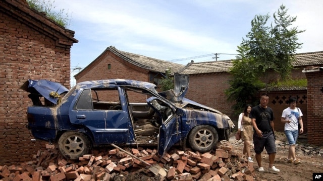 Chinese people walk past a flood-damaged vehicle sitting on the bricks at a village in Fangshan district of Beijing, China, July 23, 2012. 
