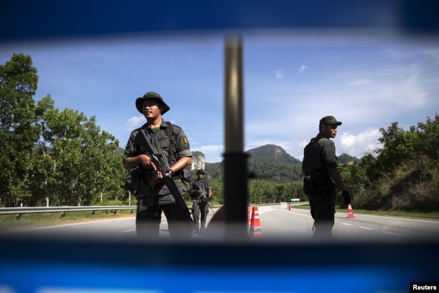 FILE - Members of the General Operations Force control the checkpoint on the road near the area where the abandoned human trafficking camp was discovered in the jungle close to the Thailand border at Bukit Wang Burma in northern Malaysia May 28, 2015.