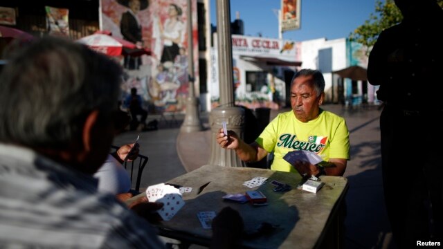 FILE - Men play cards in Mariachi Plaza in the Boyle Heights area of Los Angeles, home to many Mexican and Central American migrants, Aug. 9, 2014. Seven men have been charged in firebombings that drove blacks from their homes in the neighborhood.