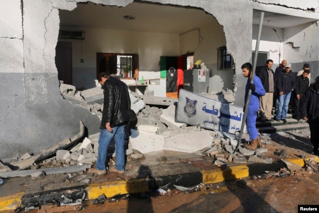 FILE - Civilians and security personnel stand at the scene of an explosion at a police station in Tripoli, Libya, a blast later claimed by militants professing loyalty to Islamic State, March 12, 2015.