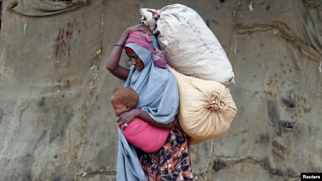 A displaced Somali woman carries a child and her belongings after fleeing famine in the Marka Lower Shebbele regions, as she arrives at a temporary dwelling in the capital Mogadishu.