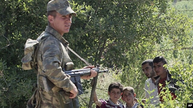 A Turkish soldier stands by as a group of Syrians wait for the authorization to enter Turkey near the Turkish village of Guvecci in Hatay province, Turkey, which borders Syria, June  9, 2011
