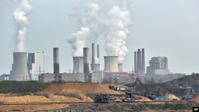 FILE - Giant machines dig for brown coal at the open-cast mining Garzweiler in front of a smoking power plant near the city of Grevenbroich in western Germany.