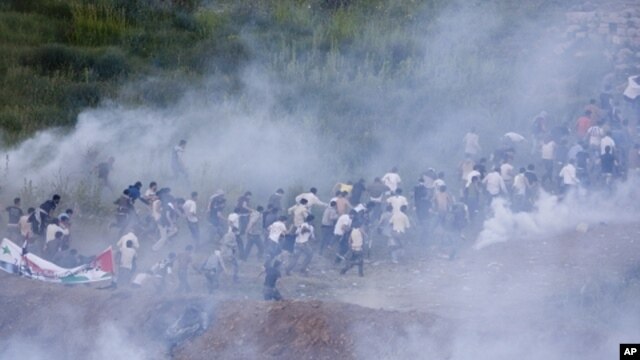 Pro Palestinians protesters run from tear gas fired by Israeli troops along the border between Israel and Syria near the village of Majdal Shams in the Golan Heights, Sunday, June 5, 2011