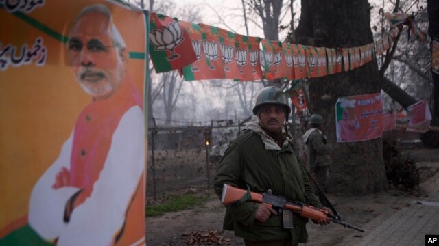 Soldados paramilitares indianos ficam de guarda do lado de fora Sheri Kashmir estádio de críquete, onde o primeiro-ministro Narendra Modi, fotografia à esquerda, é esperado para fazer discurso de campanha segunda-feira antes das eleições locais em Srinagar, Índia, domingo, 7 de dezembro, 2014.