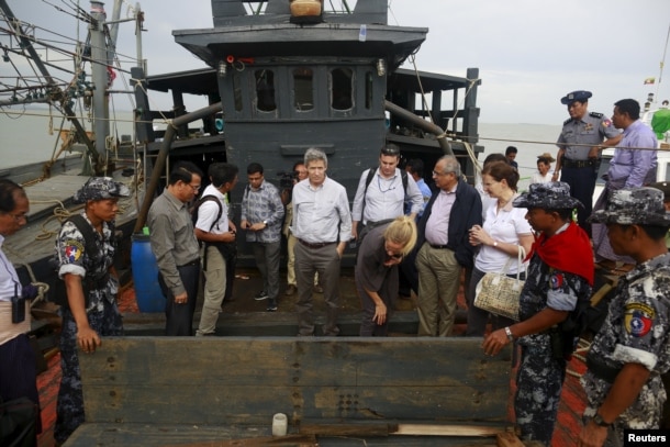 FILE - Myanmar government officials and U.N. officials stand on a boat used for human trafficking at a jetty outside Sittwe, Myanmar.