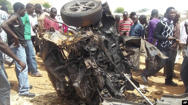 People gather around a car used by a suicide bomber following an explosion in church compound in Bauchi, Nigeria,  June 3, 2012.