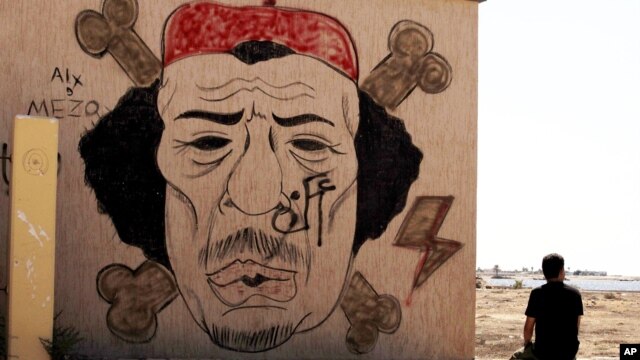 A  Libyan man sits near a mural of Moammar Gadhafi, Benghazi, September 20, 2012.