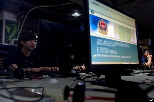 FILE - Computer users sit near a monitor display with a message from the Chinese police on the proper use of the Internet at an Internet cafe in Beijing, China.