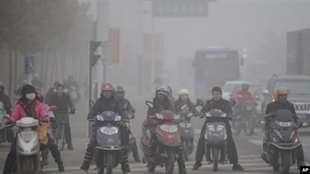 Chinese motorists ride their electric bikes in heavy fog down a street in Hefei, east China's Anhui province, 25 Nov 2009