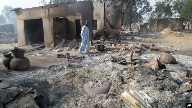 FILE - A man walks past burnt out houses following an attack by Boko Haram in Dalori village near Maiduguri, Nigeria. Abubakar Shekau says he still leads Boko Haram, exposing the biggest rift yet among Nigeria’s Islamic insurgents and possibly paving the