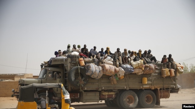 FILE - Migrants sit on their belongings in the back of a truck as it is driven through a dusty road in the desert town of Agadez, Niger, headed for Libya, May 25, 2015.  